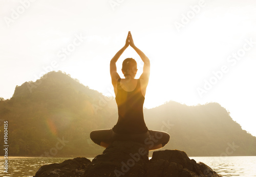 Yoga woman sitting in lotus pose on the beach during sunset (Lens Flare)