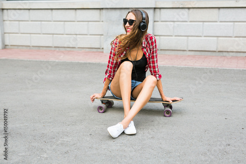 Young woman sitting on the skater. Smiling woman with skateboard in outdoors