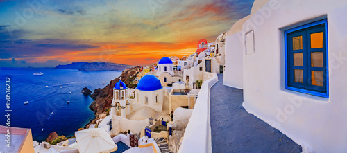 Amazing wide panorama sunset view with white houses on church with blue roofs in Oia village on Santorini island in Greece.