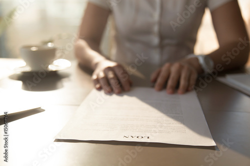 Woman sitting at the desk with loan agreement form. Close up photo of female hands lying on business document. Businesswoman reading contract terms. Financial adviser analyzing lending conditions