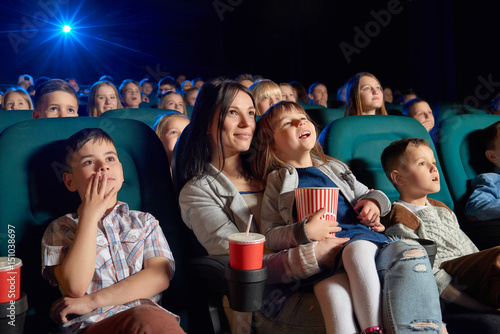 Low angle shot of people watching a movie at the cinema. Young woman and her daughter enjoying a film at the movie theatre motherhood parenting children kids entertaining happiness.