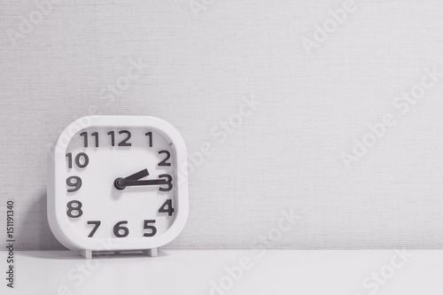 Closeup white clock for decorate show a quarter past two o'clock or 2:15 p.m. on white wood desk and cream wallpaper textured background in black and white tone with copy space