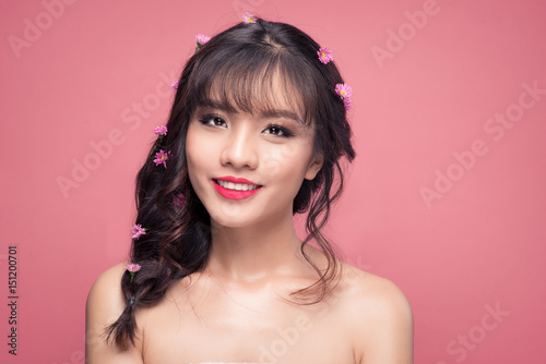 Young pretty asian woman with flowers on hair close up on pink background