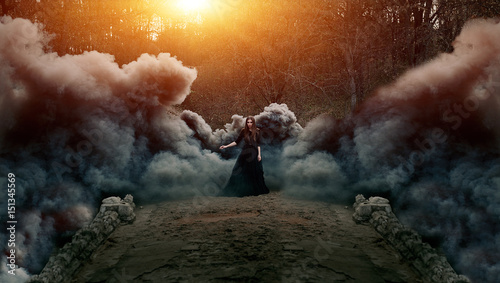 Young attractive Witch walking on the bridge in heavy black smoke.