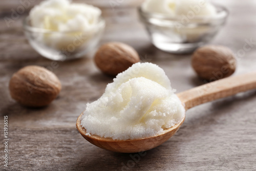 Shea butter in spoon and bowls on wooden background, close up