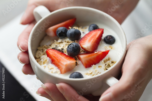 Woman hands holding bowl with tasty muesli with fruits, oat and yogurt. Closeup. Healthy Food Concept.