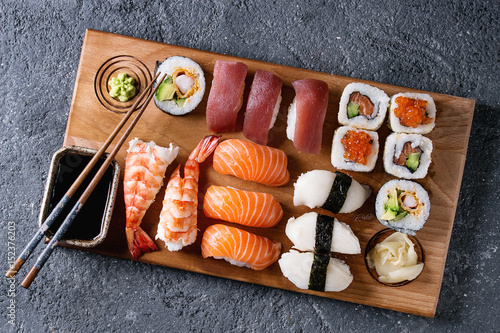 Sushi Set nigiri and sushi rolls on wooden serving board with soy sauce and chopsticks over black stone texture background. Top view with space. Japan menu