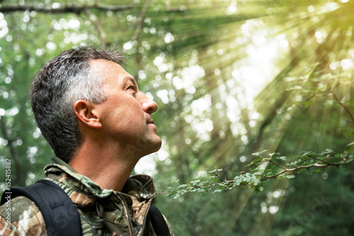 Man in forest looking at sunlight. Insight, soft focus, image toned and noise added.