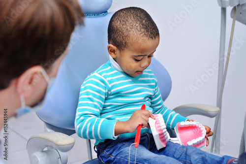 pediatric dentist man shows African boy with dark skin how to properly brush their teeth on a model of the jaw