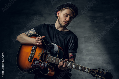 Handsome young acoustic guitar blues player with tattoos on arms.