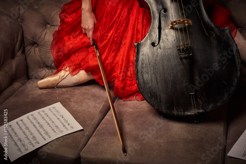 Female ballet dancer in red dress and pointe playing on antique black cello