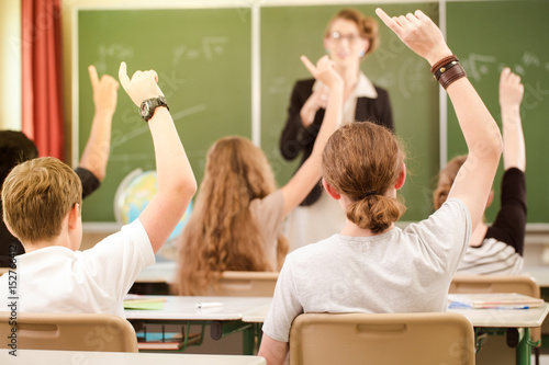 Lehrerin oder Dozent steht im Unterricht vor einer Tafel und unterrichtet Schüler, die sich melden und lernen in einer Klasse oder Schule