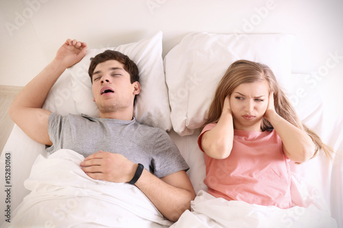Young irritated woman lying in bed with snoring husband at home