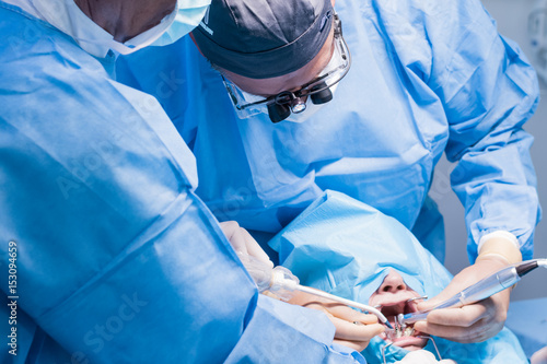 A male dentist in uniform perform dental implantation operation on a patient at dentistry office.