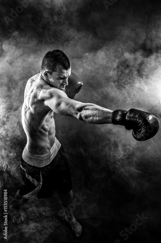 Muscular kickbox or muay thai fighter punching in smoke.