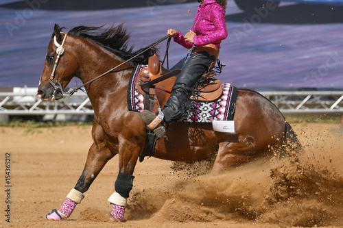 The side view of a rider in cowboy chaps and boots sliding the horse in the sand