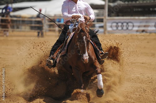 The front view of a rider in cowboy chaps and boots sliding the horse in the sand