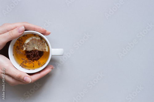 Tea time. Hands holding cup of hot black tea on the blue background, top view