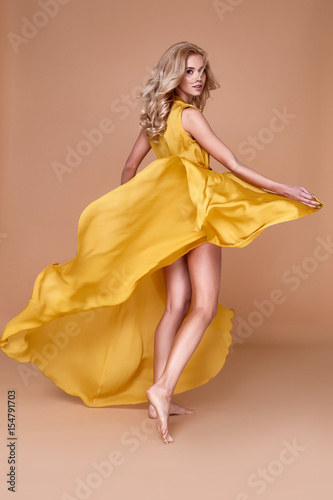 Blond hair woman beautiful face sexy skinny body shape tan skin care wear fashion dress silk yellow color runway model studio catalog clothes style for summer vacation walk date beach party makeup.