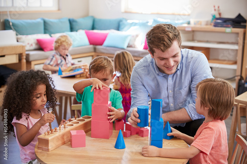 Teacher And Pupils Working At Tables In Montessori School