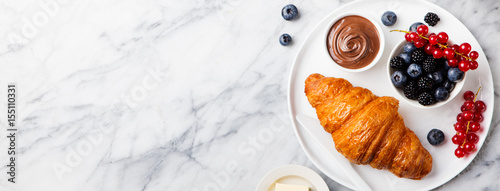 Croissant with fresh berries and butter on a marble texture background. Top view