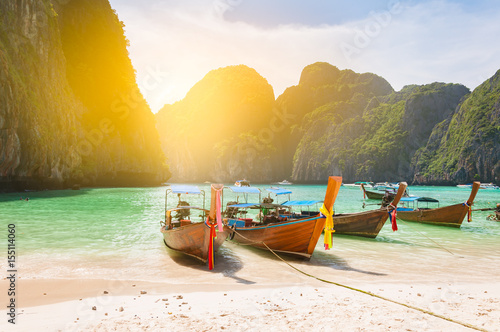 Traditional long tail boat docking in Maya bay in front of a clear and sandy beach in Krabi nearby Phuket island Thailand; light filtered