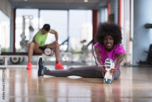 woman in a gym stretching and warming up man in background working with dumbbels