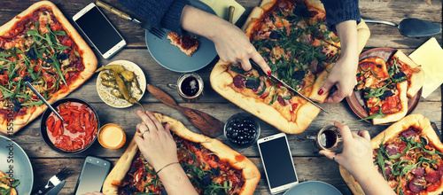 A company of people at the table enjoys dinner together with homemade pizza and various snacks. Cutting pizza, top view, rustic style.