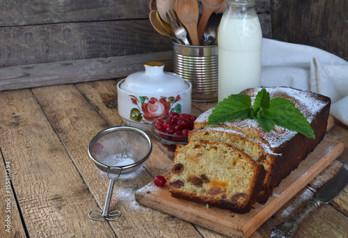 Traditional fruitcake with raisins, dried apricots, cherry for Christmas on wooden background. Sliced freshly baked cake and milk. Breakfast or afternoon snack. Copy space for text