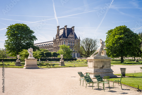 View of the Tuileries garden in Paris by a sunny morning with the statues of the Good Samaritan and Alexander Fighting in the foreground and the Flore pavilion of the Louvre palace in the background
