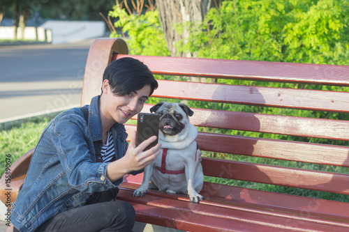 Young woman with pug make selfie on cellphone, female and dog portrait in the park