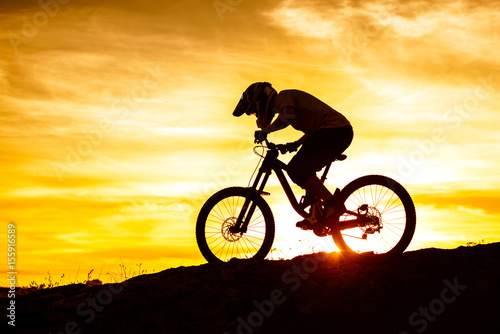 Silhouette of Cyclist Riding Down the Mountain Bike on Rocky Hill at Sunset. Extreme Sport Concept.