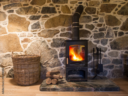 The interior of a cosy, stone cottage with stone walls and a fireplace with logs burning in a wood burner on a fireplace and hearth.