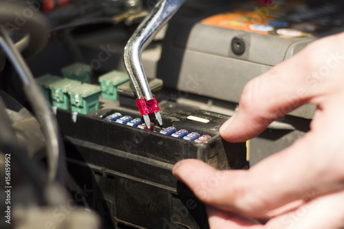 Mechanik wkłada nowy bezpiecznik do gniazda za pomocą szczypiec. Serwis samochodowy. Elektryk wymienia bezpiecznik samochodowy