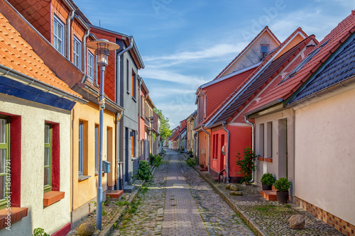 View down a historic cobble stone street with old colorful fishing cottages on a sunny day.