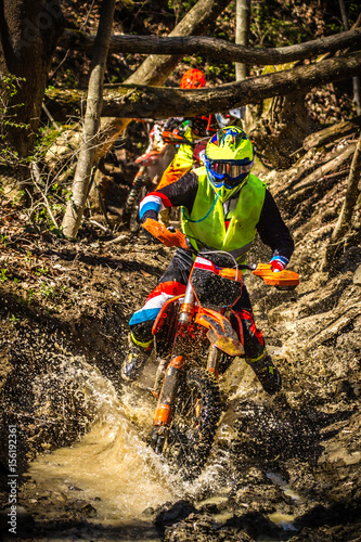 A motocross rider passes under a fallen tree on a crosscountry race