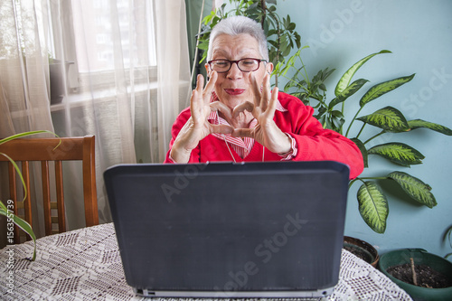 Senior old woman sending love and kisses to her family over Skype or Viber using her laptop