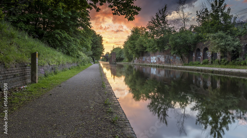 Sunset over the canal in Birmingham, UK, on a deserted footpath, with foliage flanking the tow path. The sun is creating a dramatic red and orange cloudscape in the sky