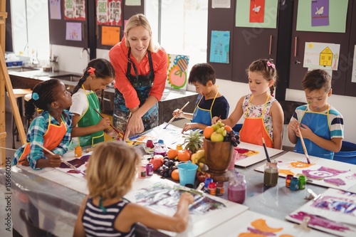 Teacher assisting schoolkids in drawing class