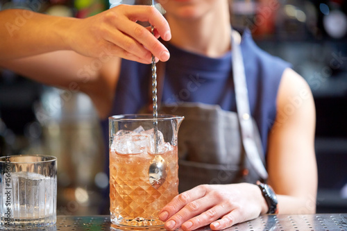 bartender with cocktail stirrer and glass at bar
