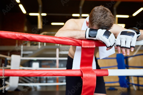 Defeated kick-boxer leaning on boxing-ring rope