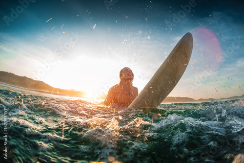 Youn happy man moves throung breaking waves in the ocean with his surf board and makes a lot of splashes