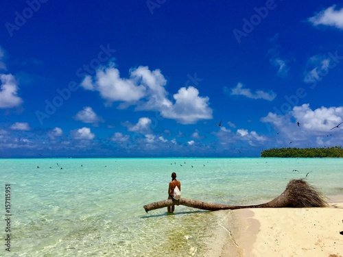 Beautiful young lady sitting on a palm tree in the turquoise lagoon of Marlon Brando's atoll Tetiaroa, Tahiti, French Polynesia