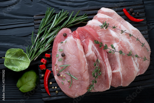 Top view of raw fresh pork loin steaks with seasonings on a black wooden background, horizontal shot