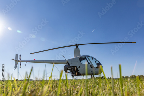 Small Robinson R22 light utility helicopter parked on grass airport. One of the world's most popular light helicopters with twin blades and a single engine