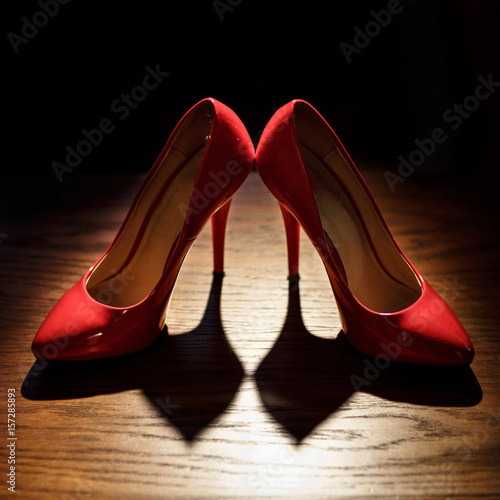 Red lacquer shoes on high heels stand on wooden table