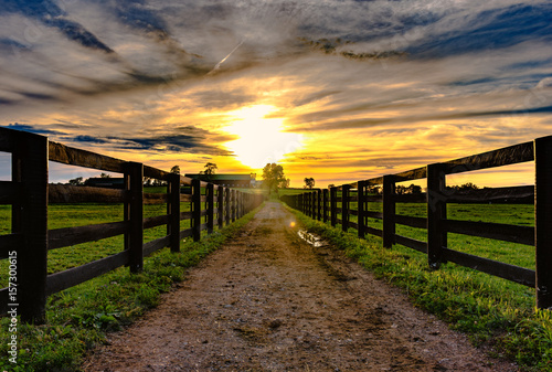 Dirt road leading to a barn with sunset in background