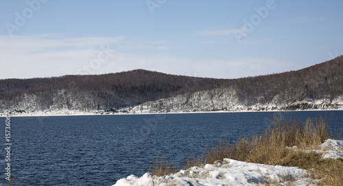 Baikal lake spring landscape view. Snow-covered shore of the lake. Rocky forested coastline.