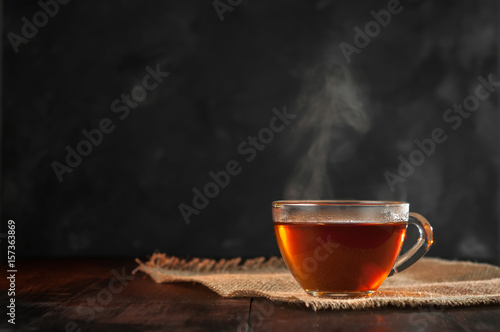 Filiżanka świeżo parzonej czarnej herbaty, ulatniająca się para, ciepłe miękkie światło, ciemniejsze tło.