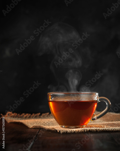 Filiżanka świeżo parzonej czarnej herbaty, ulatniająca się para, ciepłe miękkie światło, ciemniejsze tło.